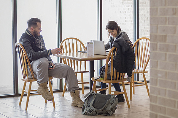 Male and female students studying at table by tall windows