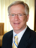 Randy Juhl is wearing a dark suit coat, white dress shirt with yellow and blue striped tie