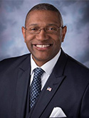 Dr. Ardrelle Evans is wearing a blue suit and tie with American flag pin