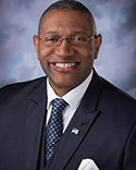 Dr. Ardrelle Evans is wearing a blue suit with tie and flag pin