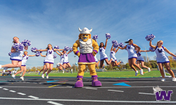 Warrick standing on asphalt track with Waldorf cheerleaders doing jumps behind him