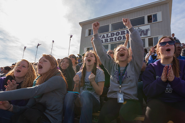 Group of female students sitting in the football stands cheering 